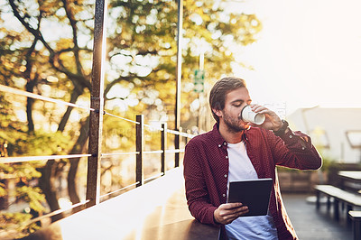 Buy stock photo Cropped shot of a handsome man using his digital tablet while drinking coffee outside