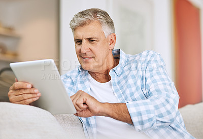 Buy stock photo Mature and senior man browsing on tablet, searching the internet and scrolling on social media while sitting on the couch at home. One retired male reading, checking and replying to messages online