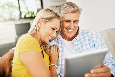Buy stock photo Happy, relaxed and in love mature couple watching a movie together on a tablet online while relaxing on a couch indoors at home. Smiling senior man and woman streaming their entertainment tv series