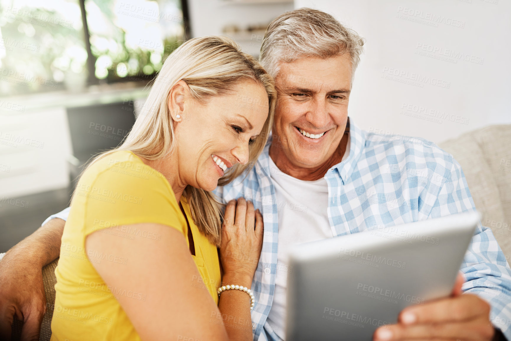 Buy stock photo Happy, relaxed and in love mature couple watching a movie together on a tablet online while relaxing on a couch indoors at home. Smiling senior man and woman streaming their entertainment tv series
