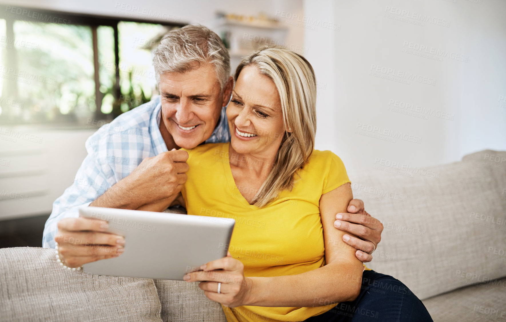 Buy stock photo Cropped shot of a mature couple using a digital tablet while relaxing at home