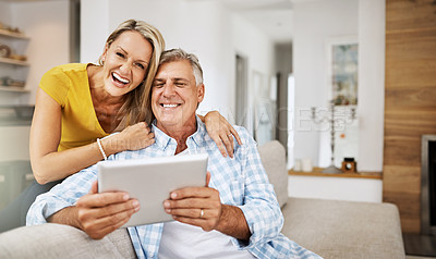 Buy stock photo Mature couple laughing and smiling at funny app on digital tablet together, on their modern living room couch. Husband and wife sitting at home and looking at their touchscreen display device