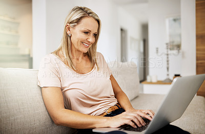 Buy stock photo Shot of a mature woman using her laptop while relaxing on her sofa at home