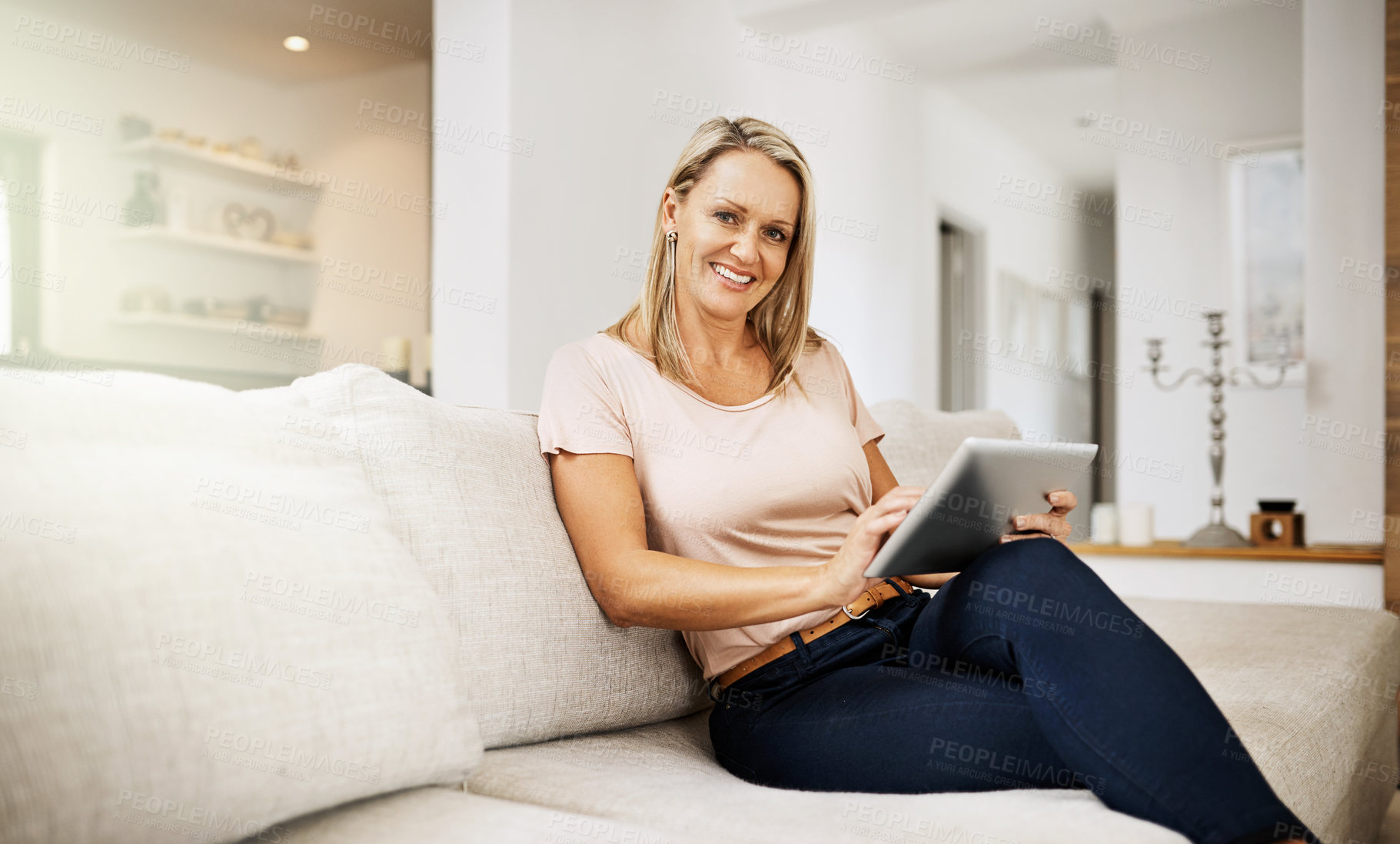 Buy stock photo Carefree and relaxed woman browsing on a tablet, enjoying her weekend and sitting on the sofa at home. Portrait of a mature comfortable, happy female surfing the internet in the living room