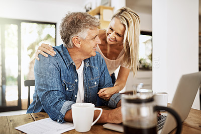 Buy stock photo Mature couple talking and browsing on a laptop while spending time together. Loving and happy wife hugging and distracting her freelancing husband while working from home at the kitchen table
