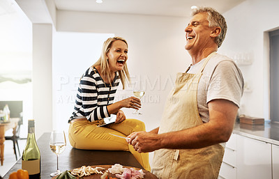 Buy stock photo Happy and carefree couple cooking dinner laughing and enjoying the weekend in the kitchen at home. A mature husband relaxing and preparing a meal or lunch for his wife while having fun 