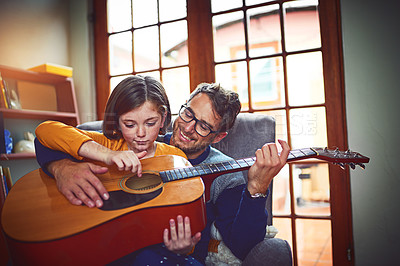 Buy stock photo Shot of a little girl playing the guitar with her father at home