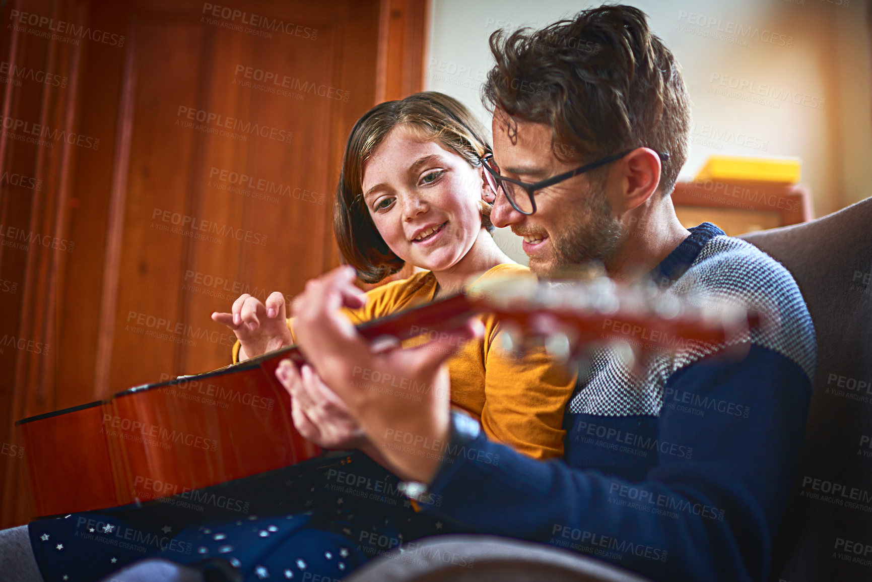 Buy stock photo Shot of a little girl playing the guitar with her father at home