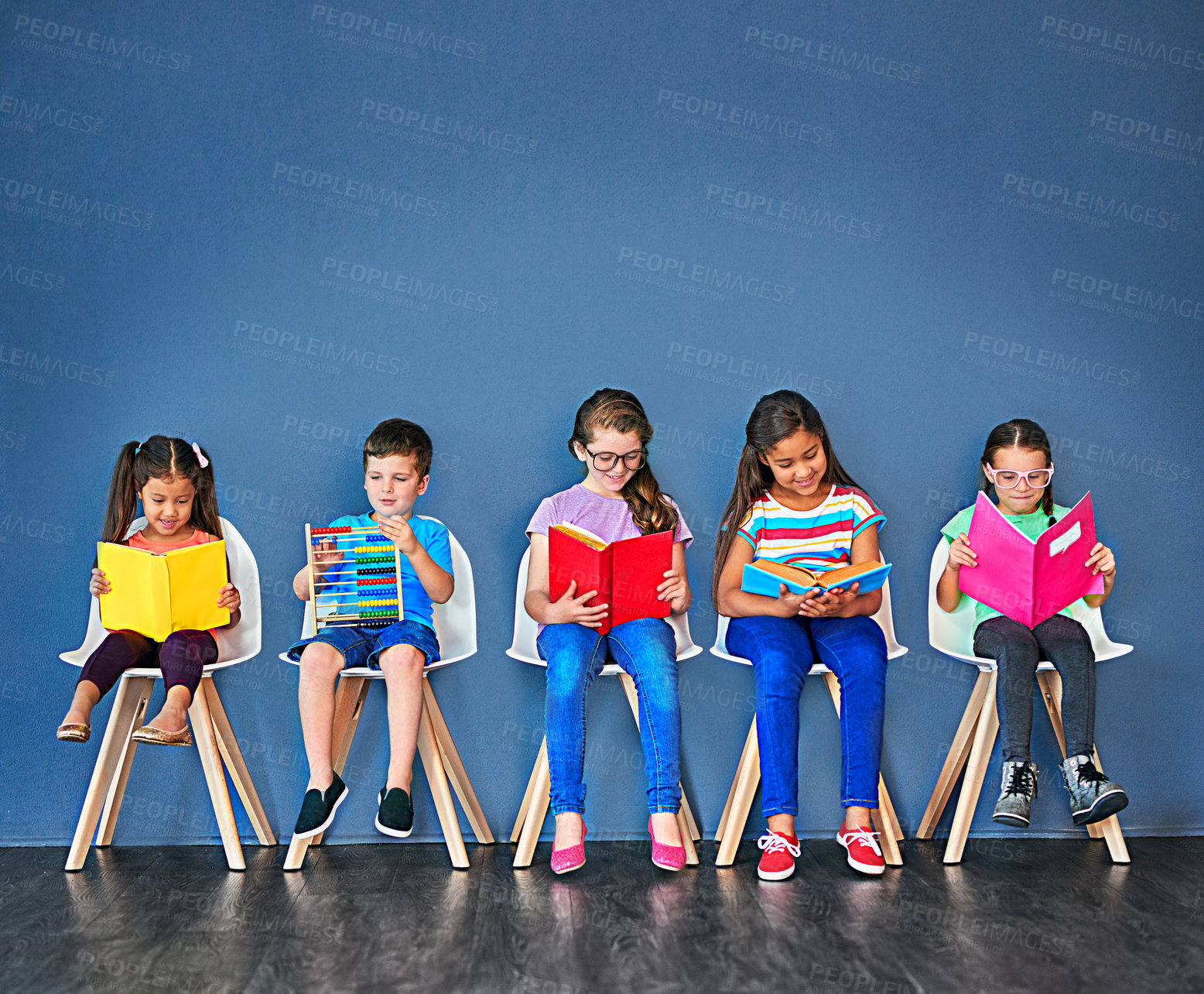 Buy stock photo Studio shot of a group of kids sitting on chairs and reading books against a blue background