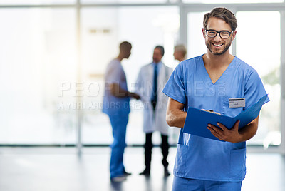 Buy stock photo Portrait of a young doctor reading the contents of a file with his colleagues in the background