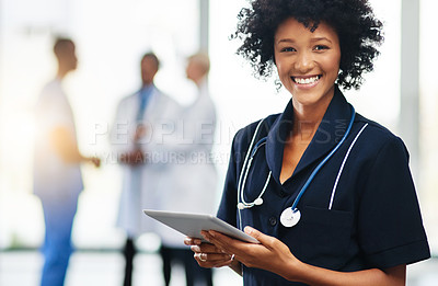 Buy stock photo Female nurse or doctor holding a tablet with colleagues standing in the background. Confident, smiling healthcare professional working with medical records on digital software app at hospital clinic
