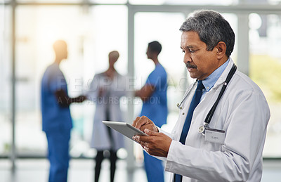Buy stock photo Focused and mature doctor browsing on a digital tablet while working in the hospital. Using wireless technology to diagnose diseases in the health medicine field. Researching medical resources online