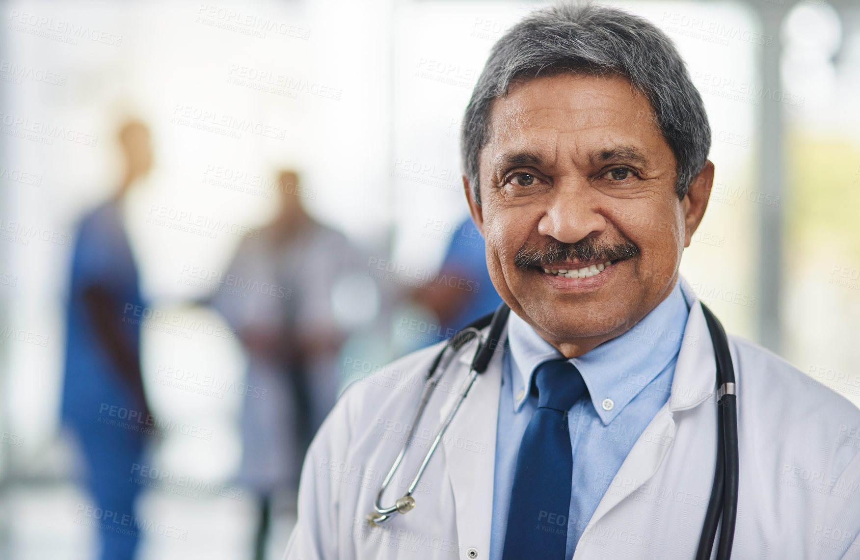 Buy stock photo Doctor, medical professional and healthcare worker with smiling, happy and friendly face expression and hospital colleagues in background. Closeup, portrait and headshot of mature clinic specialist