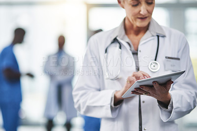 Buy stock photo Mature female doctor on a digital tablet at the hospital. Smart elderly healthcare professional woman working at a clinic. Old health expert with her work colleagues in a copy space background.