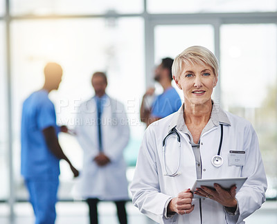 Buy stock photo Portrait of a mature doctor using a digital tablet with her colleagues in the background