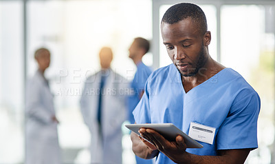 Buy stock photo Shot of a young doctor using a digital tablet with his colleagues in the background