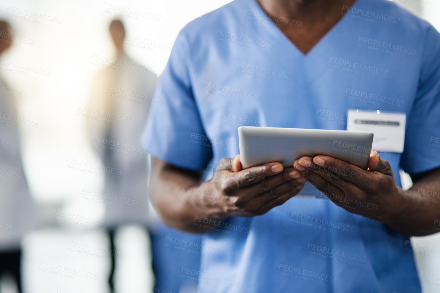 Buy stock photo Cropped shot of a doctor using a digital tablet with his colleagues in the background