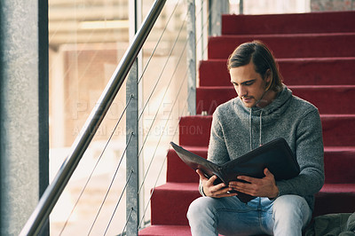 Buy stock photo Cropped shot of a handsome young university student studying while sitting on a staircase on campus