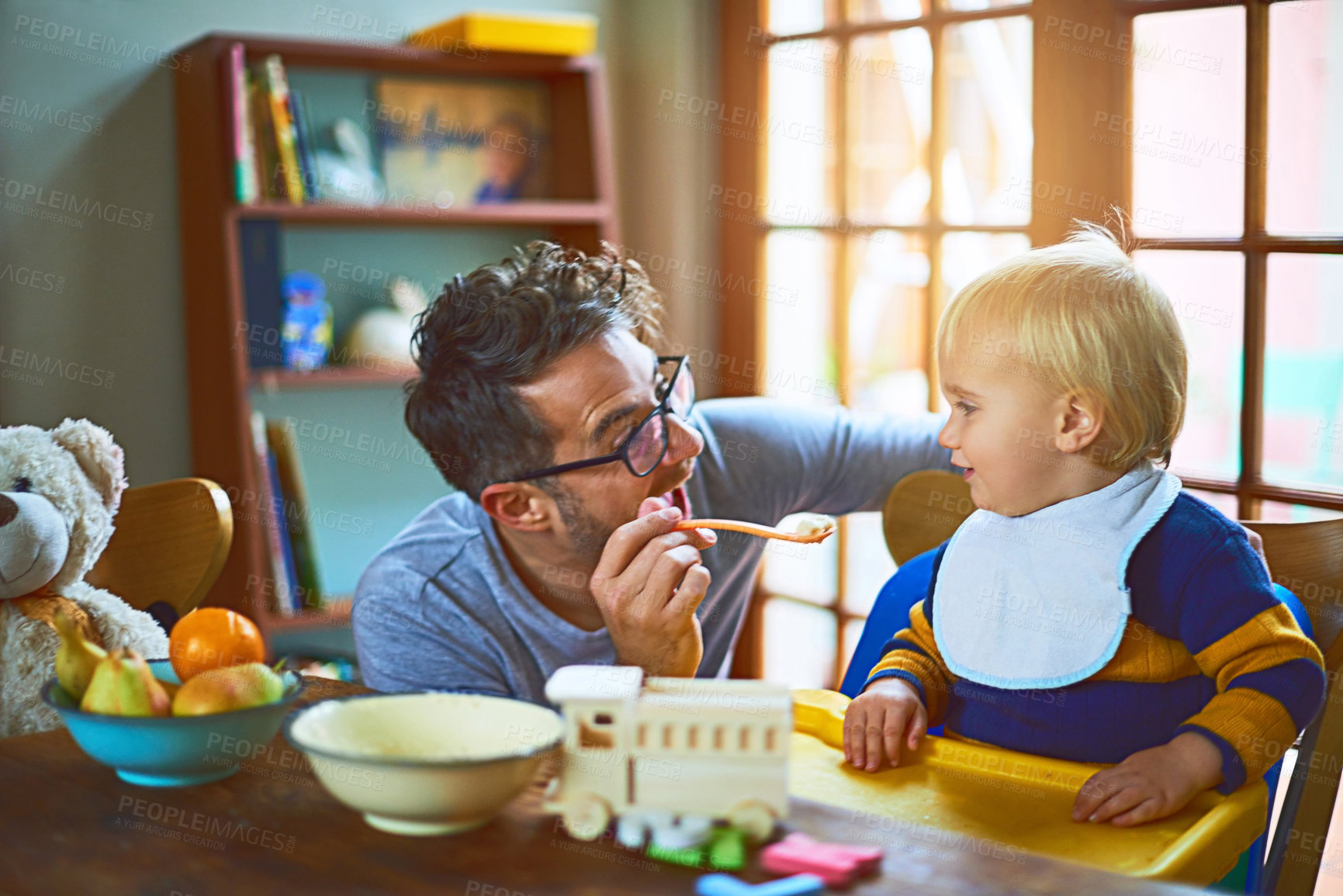 Buy stock photo Happy man, child and feeding in morning routine for bonding, love and support in home. Male person, little boy and food as family in living room for nutrition, growth and development as single parent