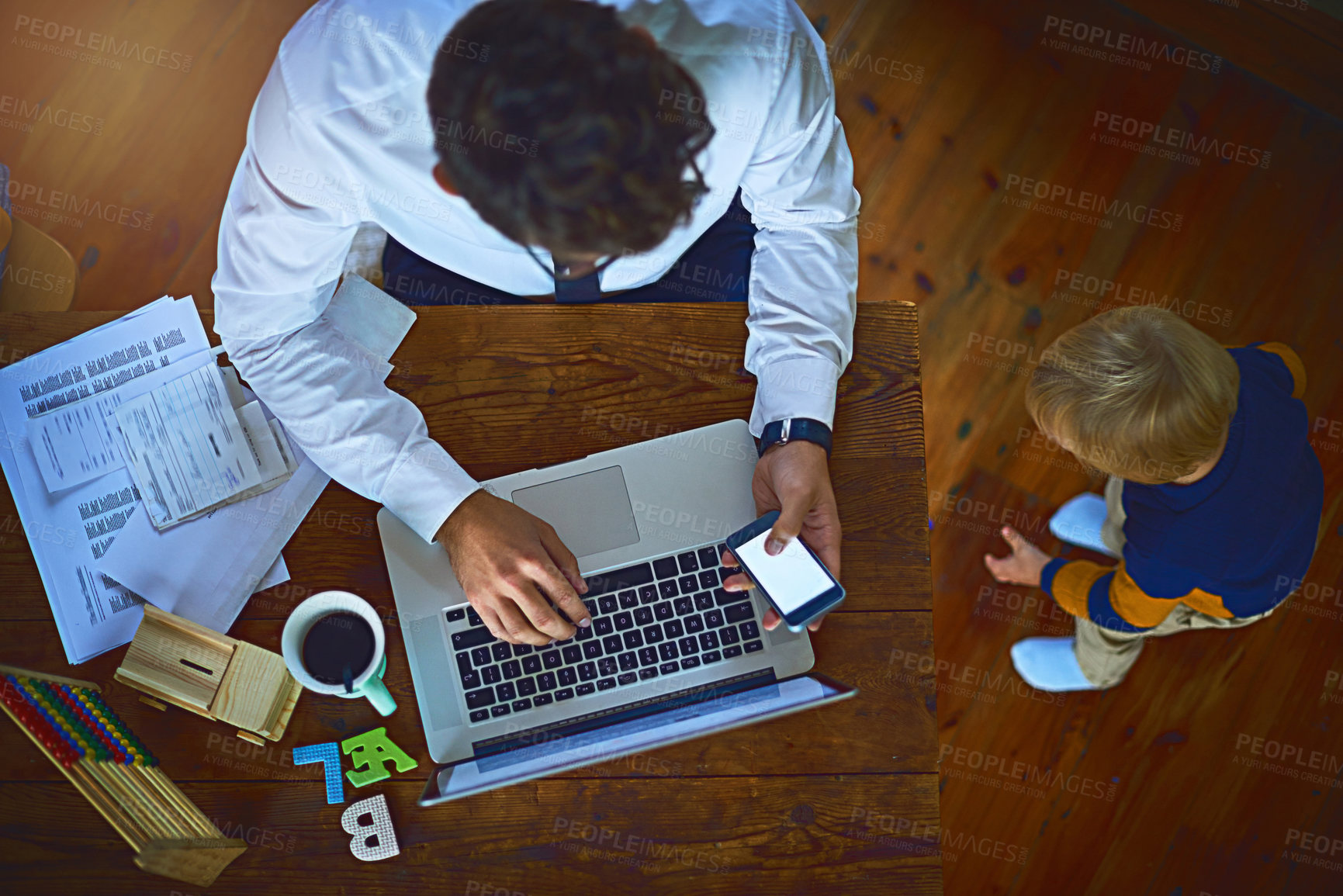 Buy stock photo High angle view shot of an unrecognizable single father using his cellphone and laptop while watching his son at home