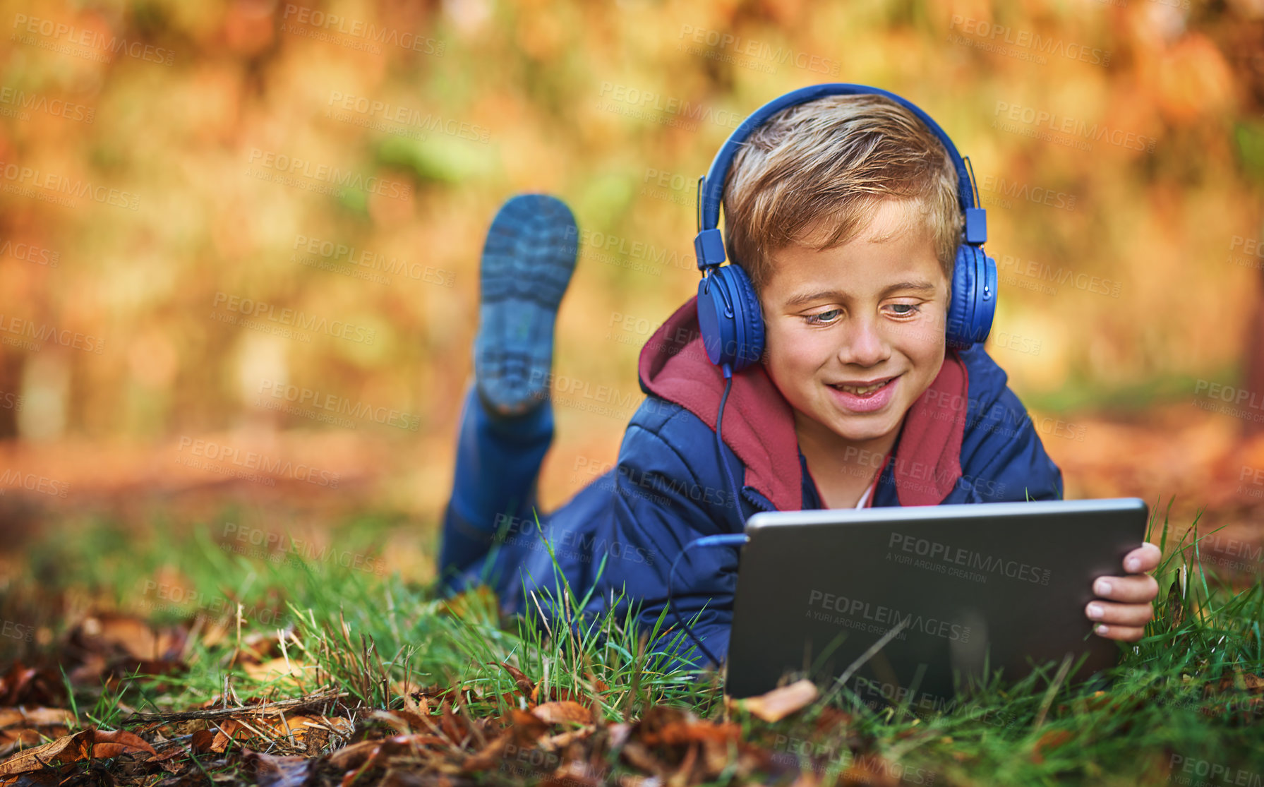 Buy stock photo Full length shot of an adorable little boy using a tablet while sitting outdoors during autumn