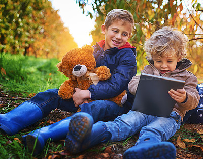Buy stock photo Cropped shot of two adorable little boys using a tablet while sitting outdoors during autumn