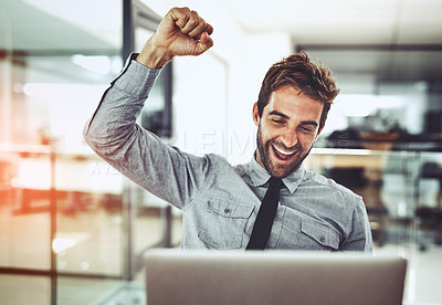 Buy stock photo Shot of a handsome young businessman doing a fist pump while working on a laptop in an office