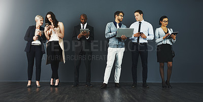 Buy stock photo Studio shot of a group of businesspeople using various digital devices against a grey background