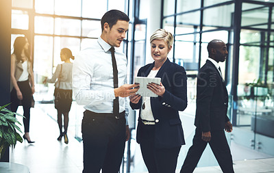 Buy stock photo Shot of two businesspeople working on a digital tablet in a busy office