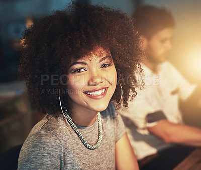 Buy stock photo Shot of a young designer working late with her colleague blurred in the background