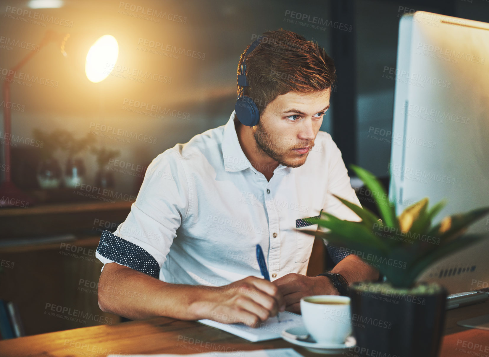 Buy stock photo Cropped shot of a young designer working late at the office while listening to music with his headphones