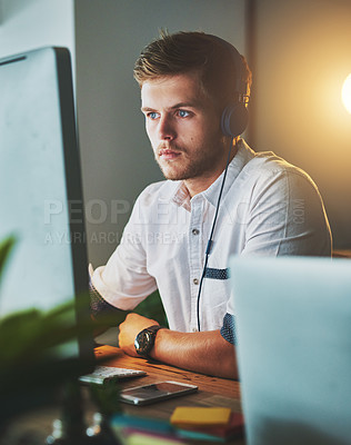Buy stock photo Cropped shot of a young designer working late at the office while listening to music with his headphones