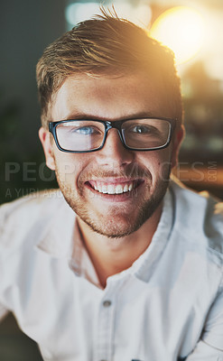 Buy stock photo Shot of a young cheerful designer working on a computer while wearing glasses in the office and looking at the camera
