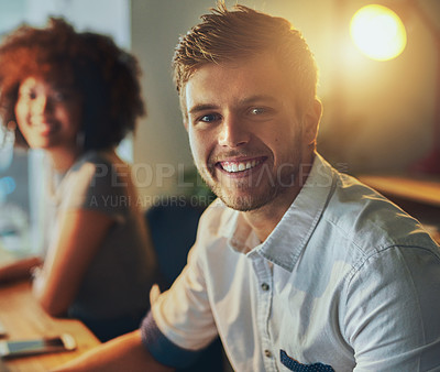 Buy stock photo Shot of two young designers working together on a computer while looking at the camera in the office