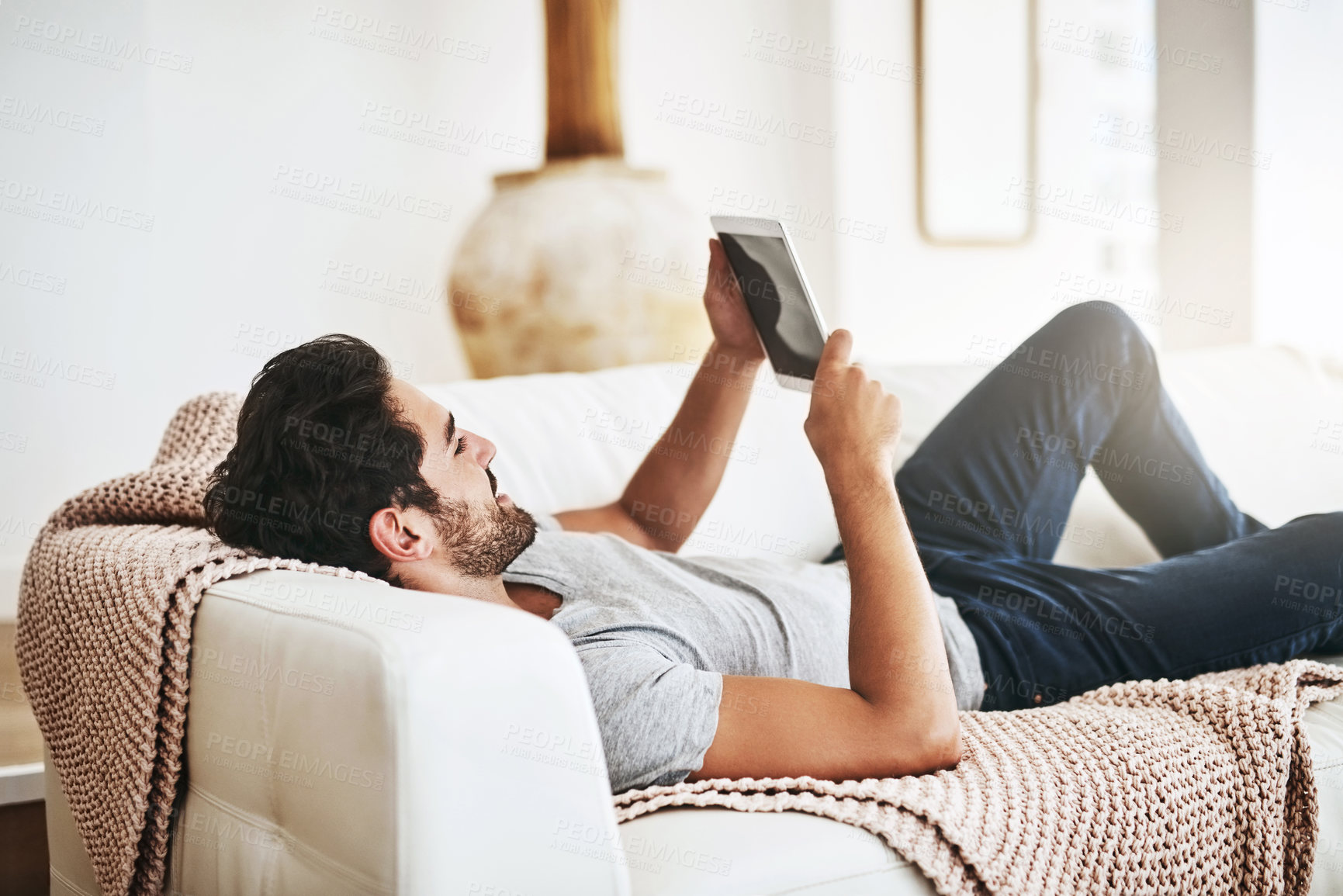 Buy stock photo App, social media and tablet with man on sofa in living room of home for streaming or weekend time off. Break, relax and technology with happy person lying on couch in apartment for rest or wellness