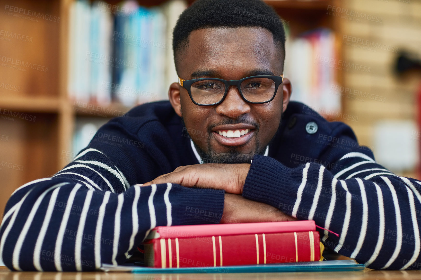 Buy stock photo African man, book and portrait at university, library and happy for studying, learning or development. Person, student and smile with laying at desk with research for assessment, exam or quiz in hall