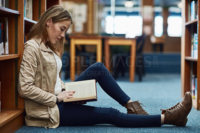 Buy stock photo Student, library and girl reading book for education, studying or literature in English, language and college. Person relax on floor by shelf with novel, knowledge or scholarship for learning history