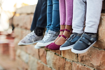 Buy stock photo Shoes, legs of school children and sitting on brick wall together. Group of friends, friendship and young student outside of classroom during lunch period or break time with footwear showing.