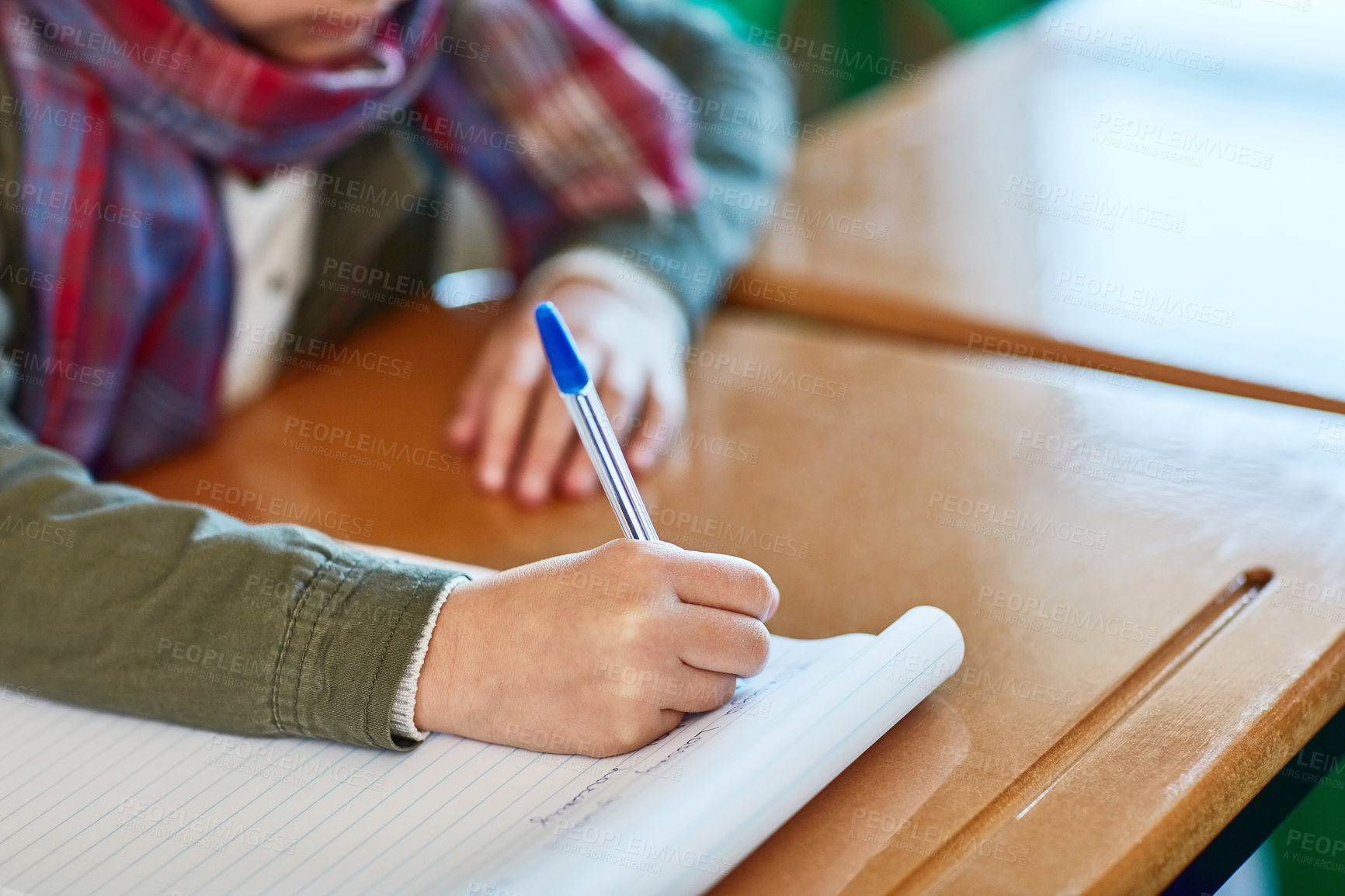 Buy stock photo Cropped shot of an unrecognizable elementary school girl writing in a workbook in the classroom