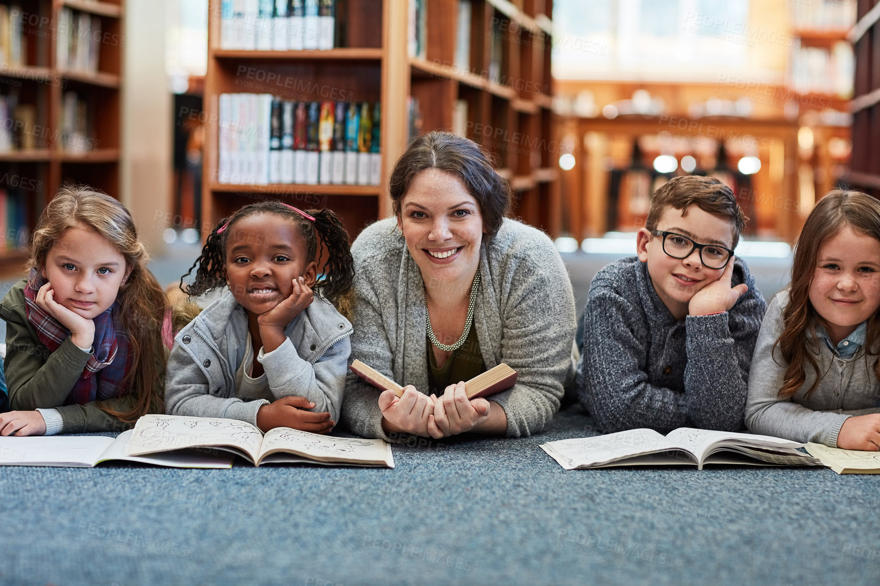 Buy stock photo Cropped shot of elementary school kids reading with their teacher on the floor in the library