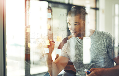 Buy stock photo Shot of a man writing ideas on sticky notes with his team behind him