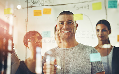 Buy stock photo Professional, happy and creative businesspeople brainstorming a strategy idea and writing on sticky notes on a transparent board with colleagues. Diverse group planning and working together in a team