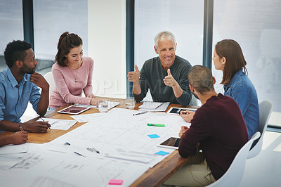 Buy stock photo Cropped shot of a group of architects looking over blueprints during a meeting in the boardroom
