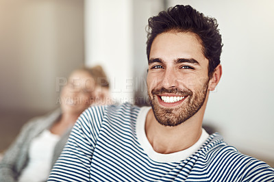 Buy stock photo Shot of a young man sitting at home with his girlfriend in the background
