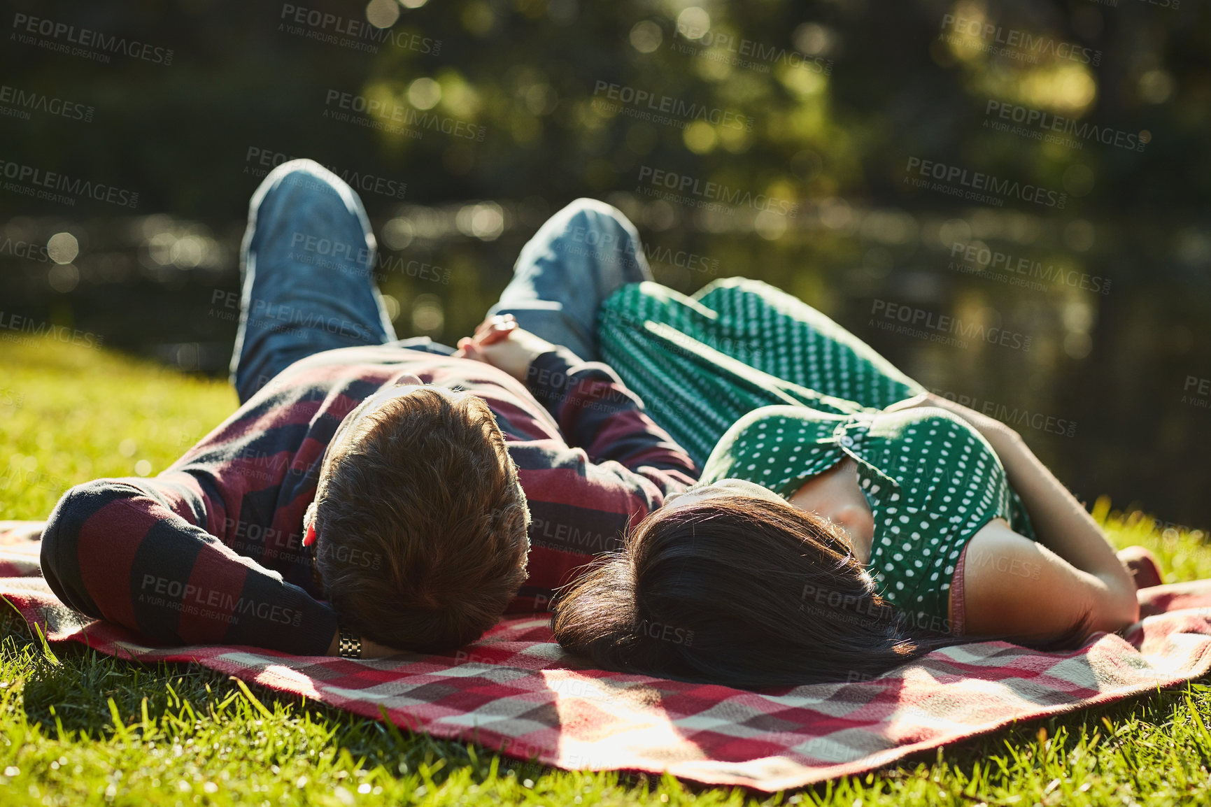 Buy stock photo Couple, lying and blanket for by lake at park with care, love and bonding on grass in spring sunshine. Man, woman and outdoor together with connection, holiday or relax by water for date in nature