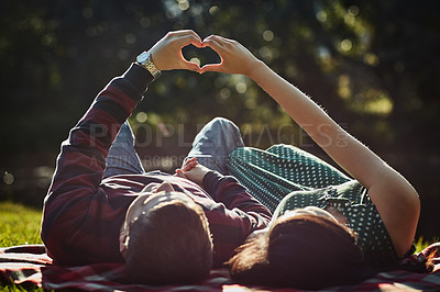 Buy stock photo Shot of a young couple lying together on the grass and making a heart gesture with their hands