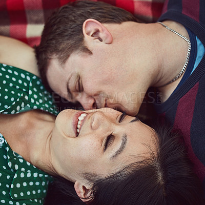 Buy stock photo Shot of an affectionate young couple relaxing together on a picnic blanket