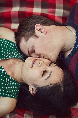 Buy stock photo Shot of an affectionate young couple relaxing together on a picnic blanket