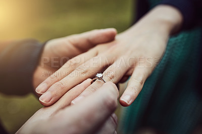 Buy stock photo Cropped shot of a man putting an engagement ring onto his fiancee’s finger outdoors