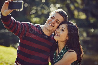 Buy stock photo Shot of a happy young couple taking a selfie together in the park